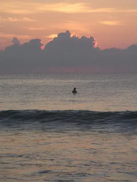 Sunset over the water at Arugam Bay with a surfer in the lineup